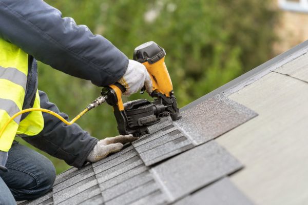 Close-up of worker installing asphalt roof shingles during repair