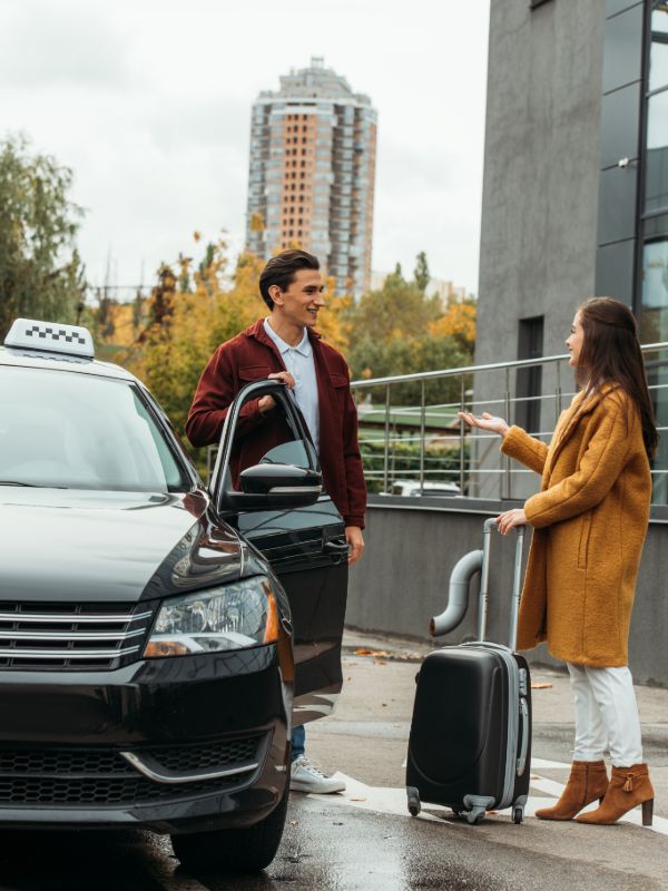 Airport taxi driver picking up customer with luggage