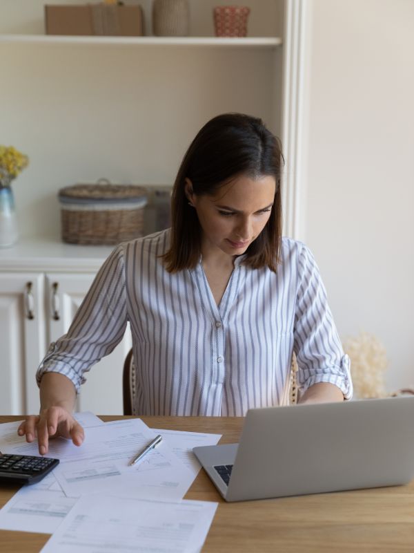 bookkeeper reviewing financial documents and working on laptop