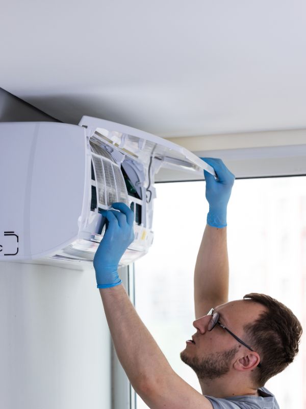 AC technician servicing a wall-mounted air conditioning unit inside a home