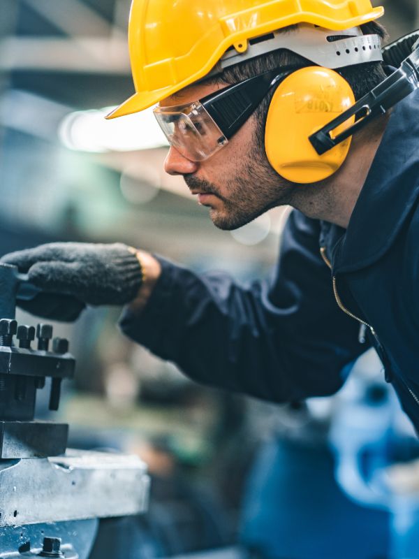 Factory worker inspecting metal component with safety gear in manufacturing unit
