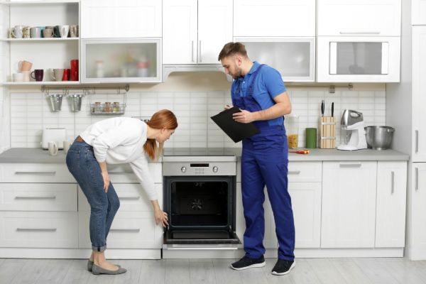 Technician inspecting a kitchen appliance with a customer