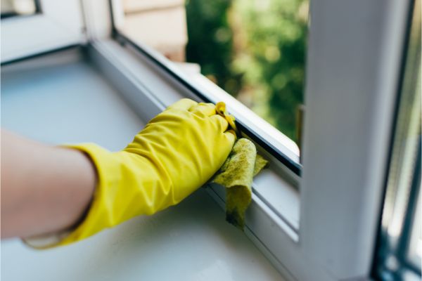 Cleaning a residential window frame with protective gloves and cloth